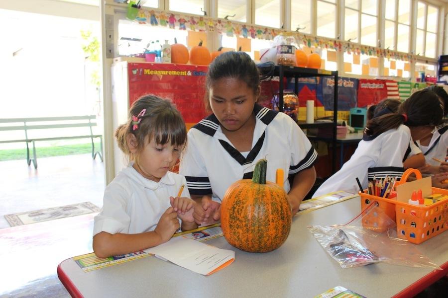 “Big sister” Mercedes Anacleto helps “little sister” Isabella Miljkovic use math skills to measure a pumpkin. 