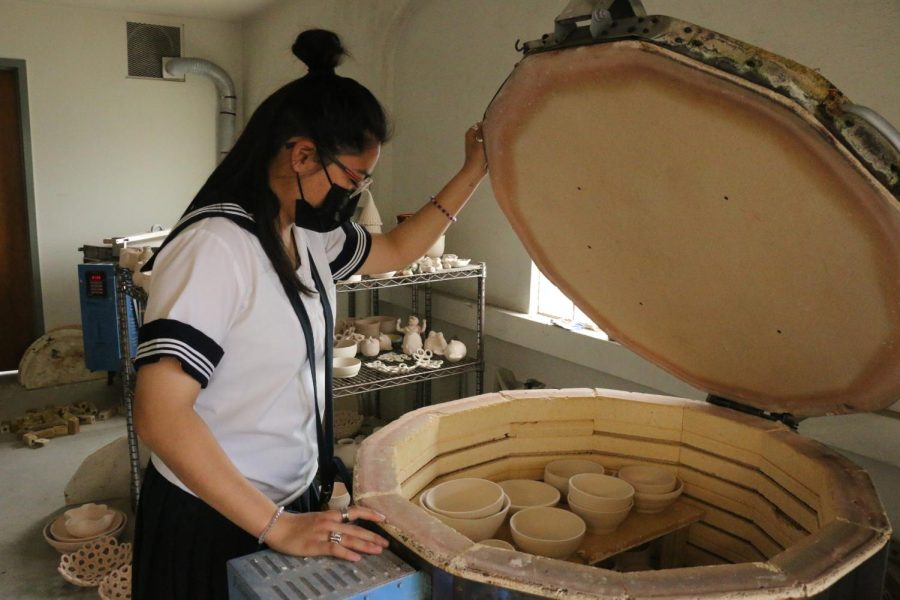 Senior Ariana Oshiro peaking into the kiln to view her latest creations. This is the first stage of firing, called bisque firing. A kiln is a special oven used for firing pottery and ceramic pieces. Photo courtesy of Ember-Joy Guevarra.